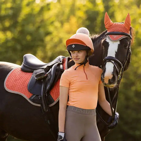 Orange and black equestrian helmet with a white pom-pom on top