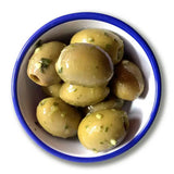 A bowl of glossy greenish yellow delphi stuffed green olives with chopped herbs garlic in organic chilli garlic basil style