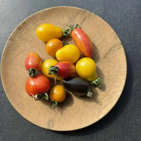A rustic wooden plate with organic heritage cherry tomatoes in vibrant yellow red and striped varieties