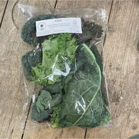 A package of fresh organic kale with dark green curly leaves and a white label from a certified farm equestrian quality
