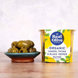 A vibrant yellow and green container of organic lemon thyme and black pepper pitted green olives from the real olive company