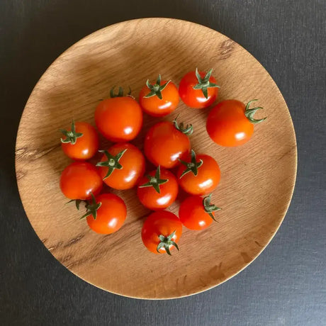 A cluster of vibrant organic red cherry tomatoes with green stems on a rustic wooden plate hand grown and fresh