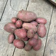 A pile of fresh organic red potatoes with earthy red skins resting on a weathered wooden surface