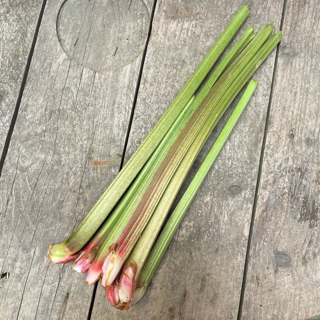 Fresh organic rhubarb stalks with pinkish red bases arranged on a weathered wooden surface for natural use
