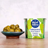 A vibrant green and white 150g container of organic wild garlic and basil pitted green olives from the real olive company