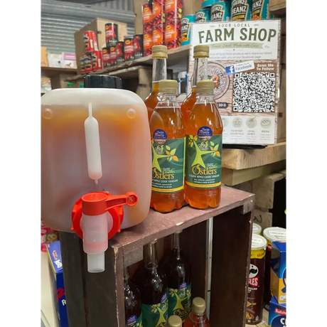 Translucent plastic dispenser with red spigot filled with amber ostlers cider organic apple cider vinegar mother refills north devon