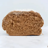 A dense dark brown pantique bread loaf with coarse crust and visible seeds unlike typical round white bread
