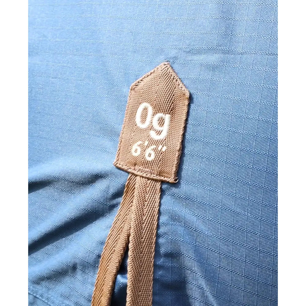 Brown woven fabric tag on blue textured fabric of perf combo 0g lightweight turnout rug for horses
