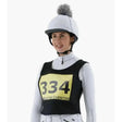 White equestrian helmet with gray faux-fur pom-pom paired with premier equine lycra vest competition bib