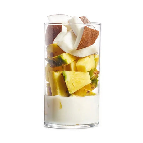 A clear glass cup with layers of white yogurt pineapple chunks and coconut pieces in the projuice coconut crush smoothie