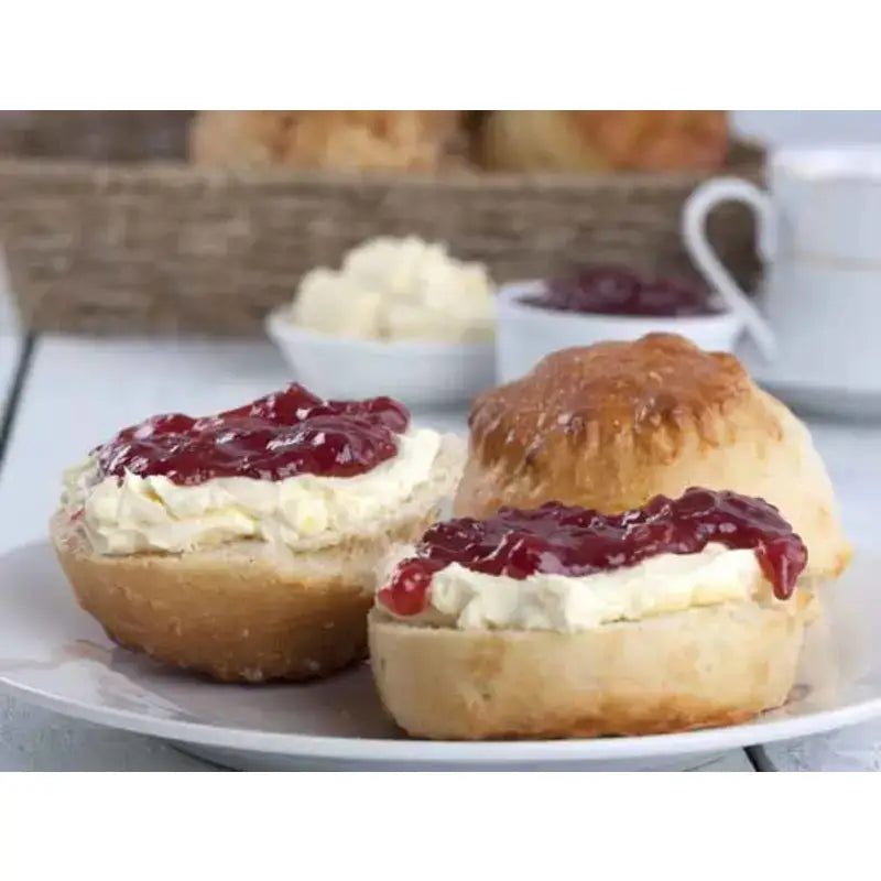 Golden-brown proper devon scone halves topped with creamy clotted cream and red jam on a white plate
