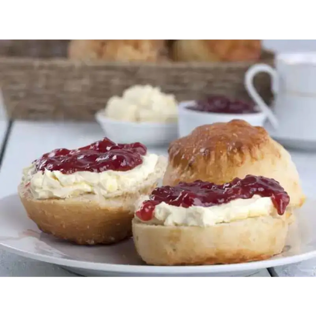Golden-brown proper devon scone halves topped with creamy clotted cream and red jam on a white plate