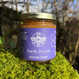 A jar of queens north devon heather honey with amber honey inside a purple label and gold lid