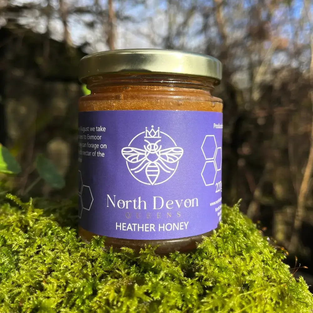 A jar of queens north devon heather honey with amber honey inside a purple label and gold lid