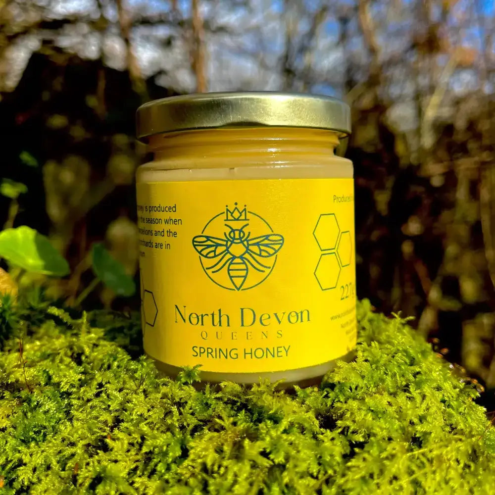 A vibrant yellow jar of queens north devon spring honey sealed with a metallic lid and bee motifs on the label