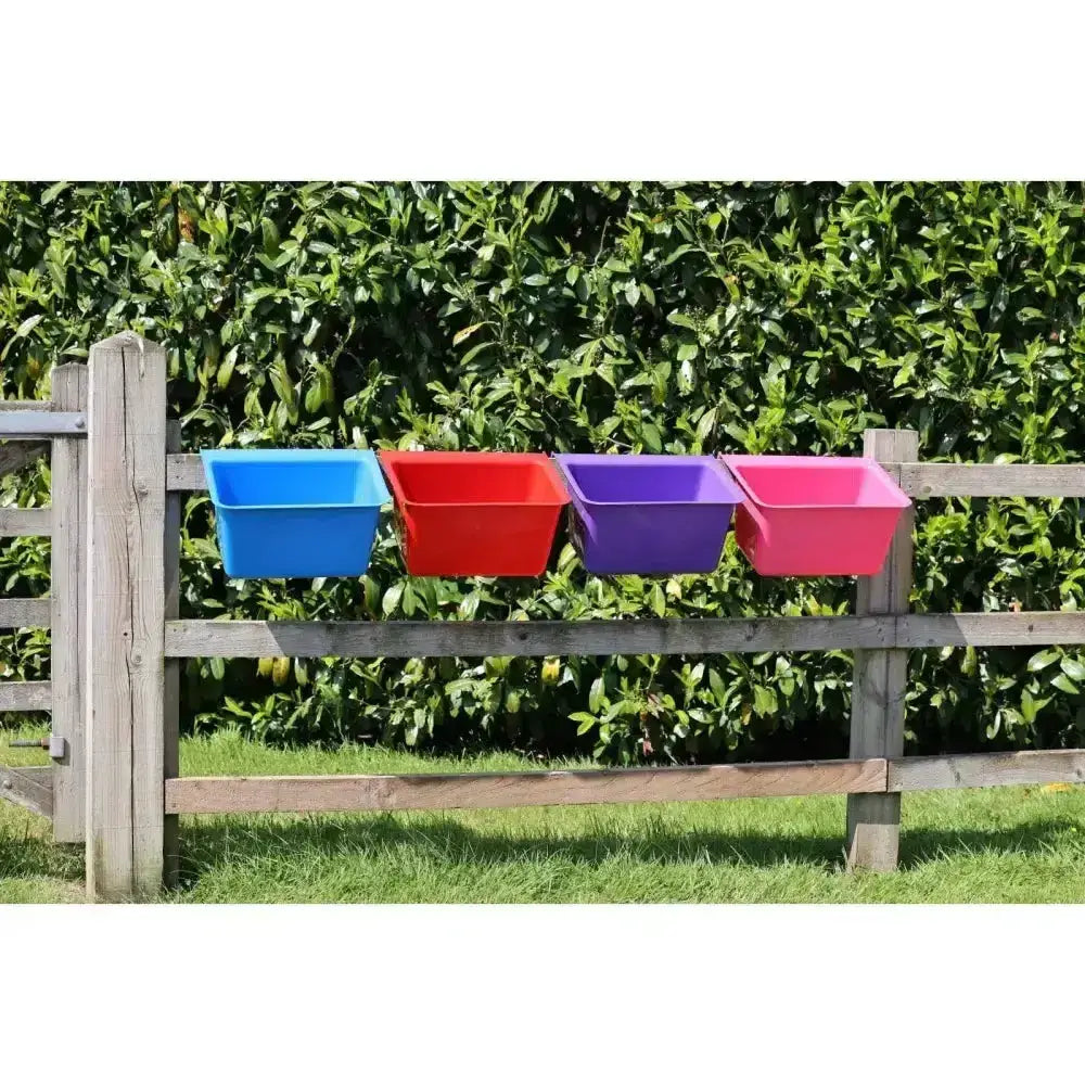 Four brightly colored plastic gorilla plas manger feed troughs in blue red purple and pink mounted on a wooden fence