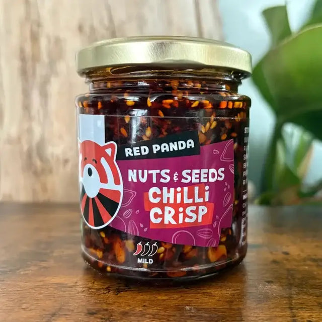A glass jar of red panda seeds chilli crisp with a gold lid and a vibrant purple label featuring the red panda logo