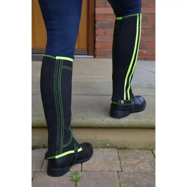 Black reflector half chaps with neon green stripes, ribbed texture, and adjustable strap closure by hy equestrian