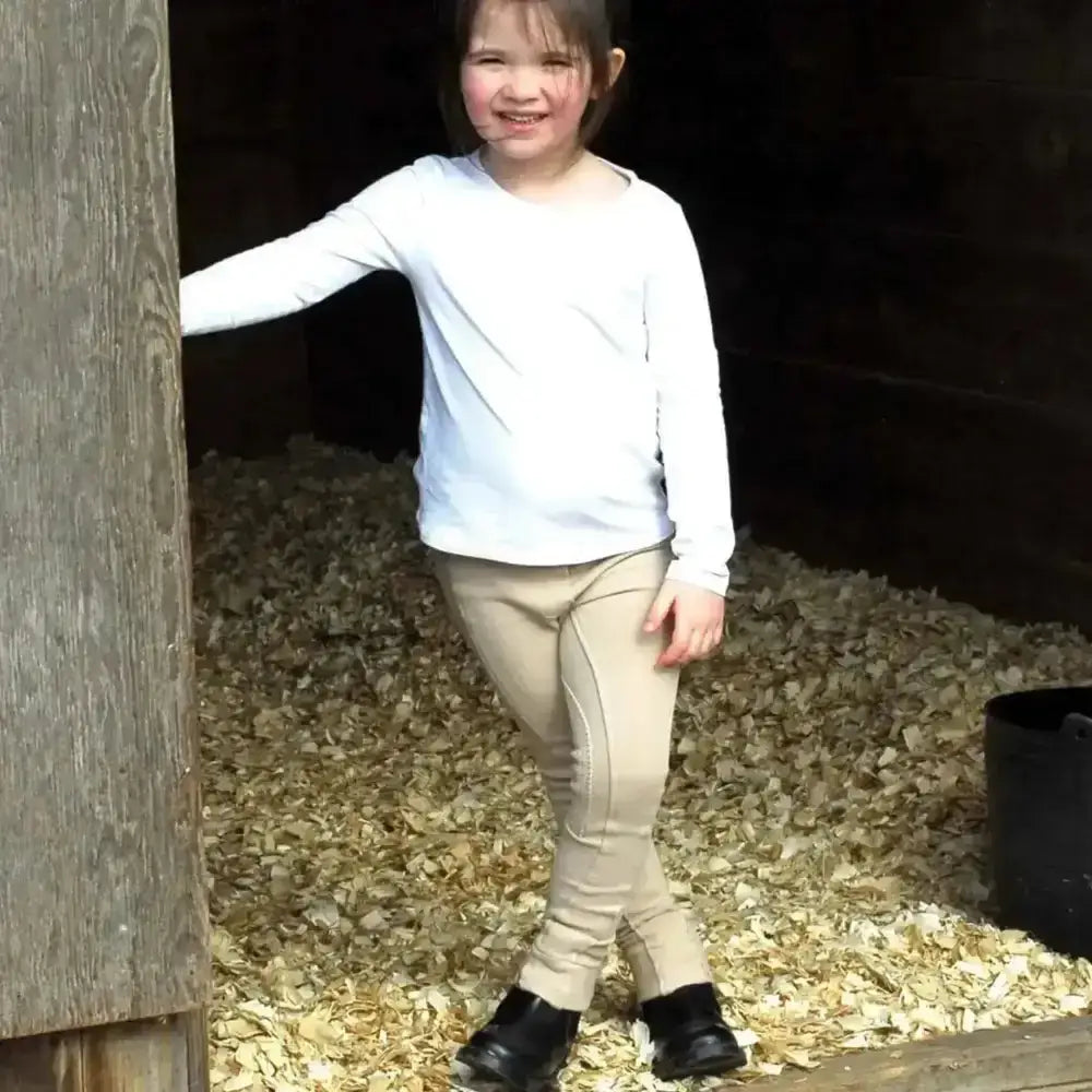 A young girl wearing beige rhinegold childs jodhpurs essential everyday with inside pocket and black boots