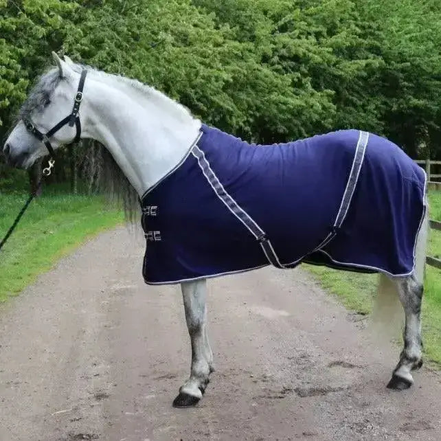 A navy blue rhinegold comfey fleece rug with white trim and black buckles made from anti-pill material fits snug on horse