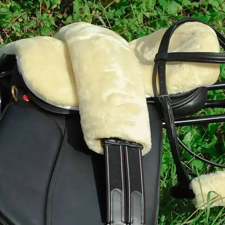 Cream-colored sheepskin rhinegold luxury seat saver with black leather straps on a black equestrian saddle