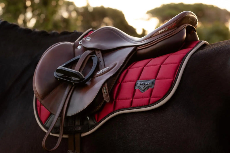 A rich burgundy quilted saddle pad with a sleek black leather riding saddle resting atop it.