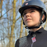 Black equestrian helmet with subtle pink logo featuring rider emergency tag for emergency contacts and medical details