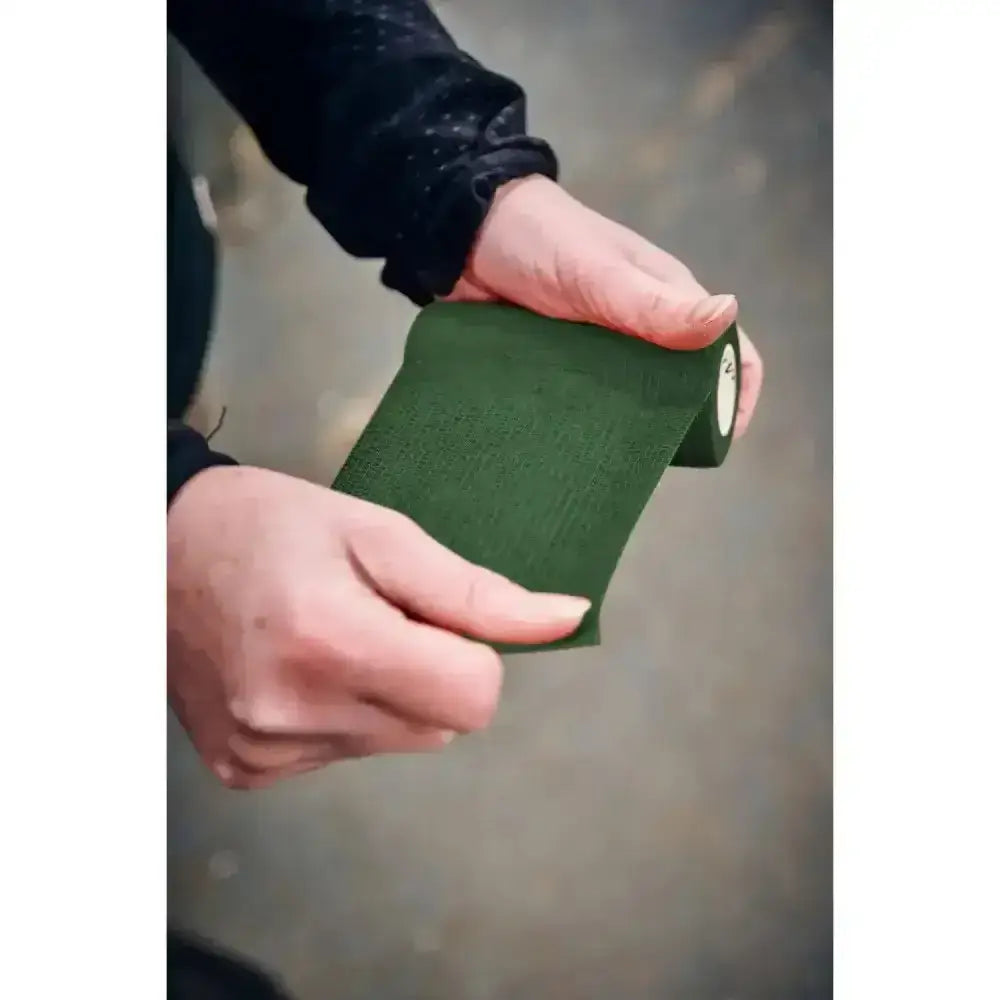 Dark green robinsons healthcare equiwrap bandage roll held in hands perfect for vet wrap robinsons use