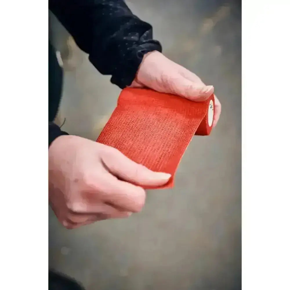 Hands holding bright red textured robinsons healthcare equiwrap bandage vet wrap for secure support