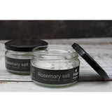 Clear glass jar with black lid containing rosemary herb infused salt by broomhill farm co for seasoning meals
