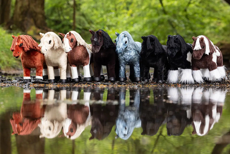 A row of plush ponies in various colors and patterns, including solid hues like red, white, brown, black, and blue with speckled or pinto markings.