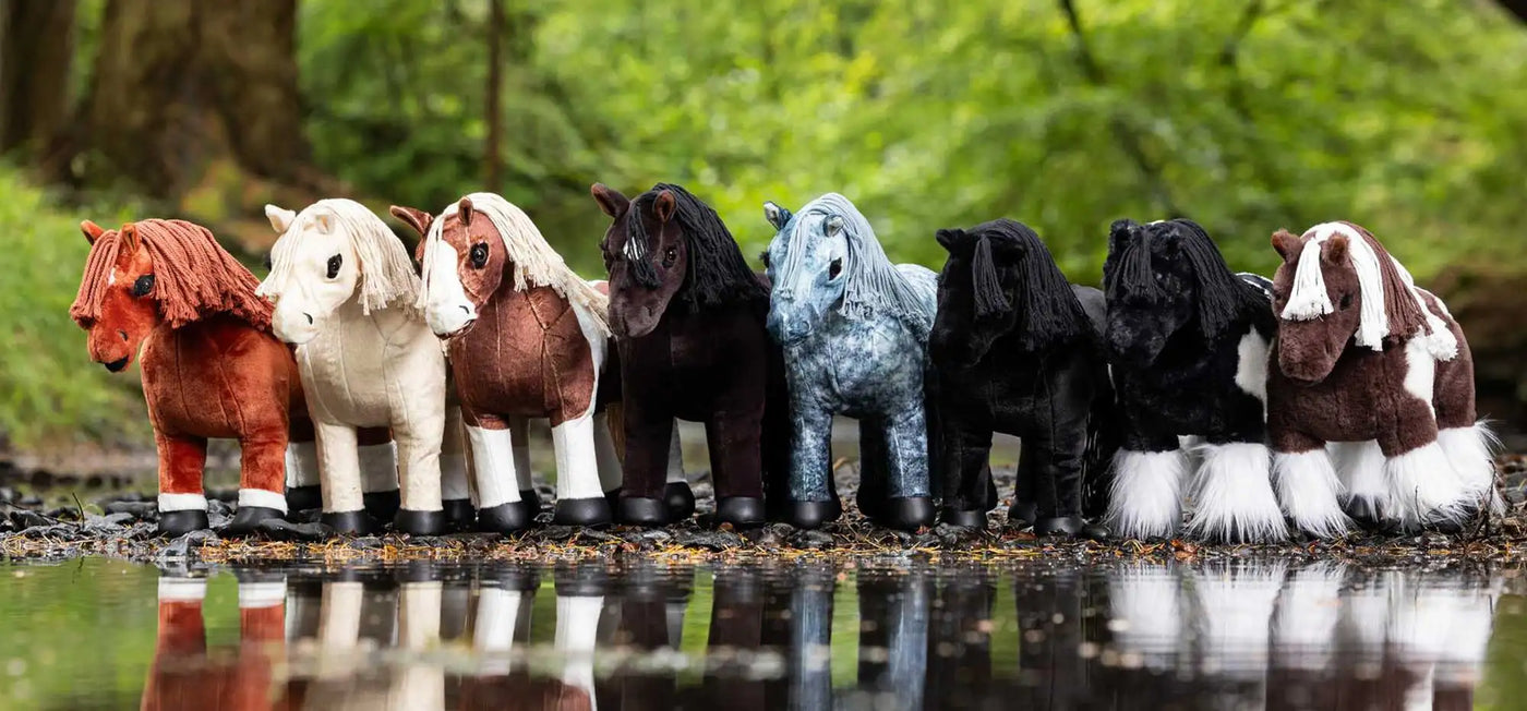 A row of plush ponies in various colors and patterns, including solid hues like red, white, brown, black, and blue with speckles or stripes.