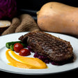 Grilled rump steak with sear marks served with purple cabbage cherry tomatoes green beans and vibrant orange sauce