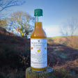 A clear glass bottle with green cap containing amber schniffells botanical cordial infusion drink labeled the exmoor elixir