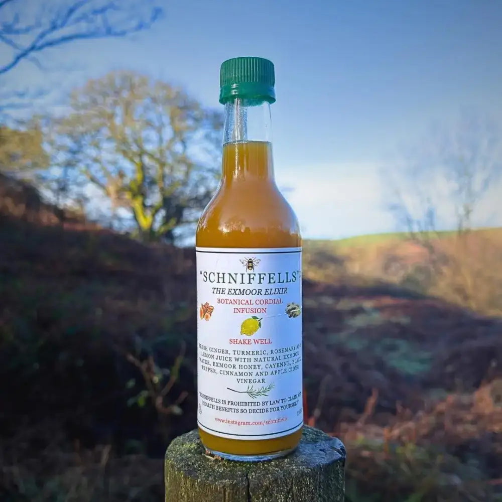 A clear glass bottle with green cap containing amber schniffells botanical cordial infusion drink labeled the exmoor elixir