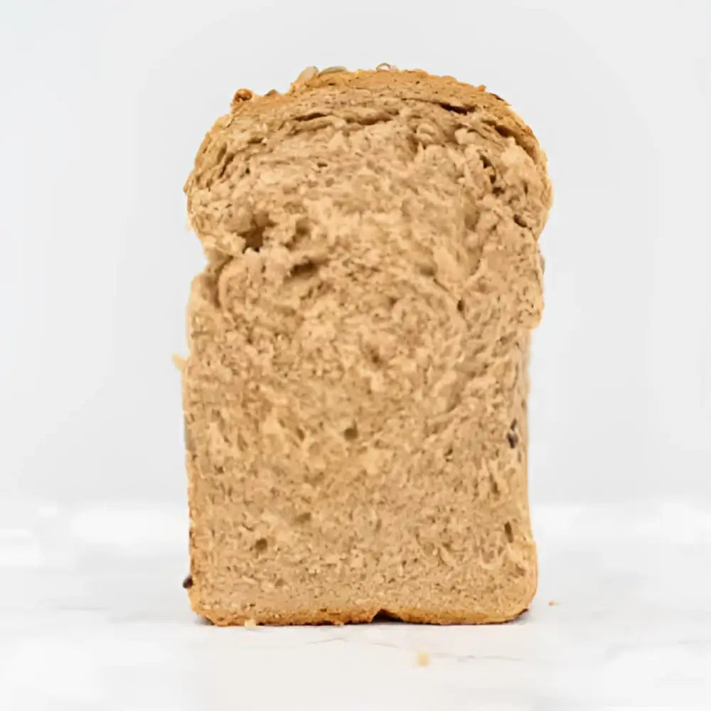 A slice of seeded rye bread with a dense textured interior and golden crust from a round loaf