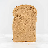 A slice of seeded rye bread with a dense textured interior and golden crust from a round loaf