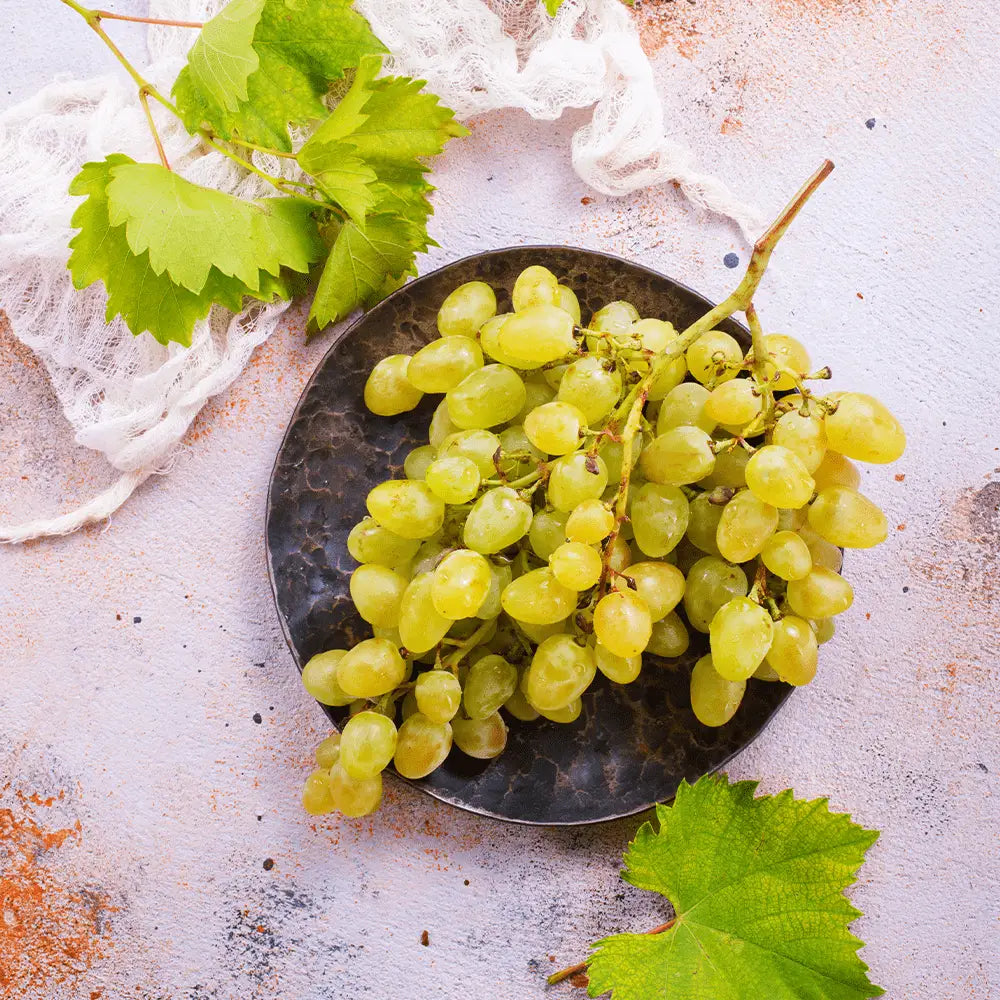 A cluster of fresh seedless white grapes resting on a dark textured plate perfect for snacking