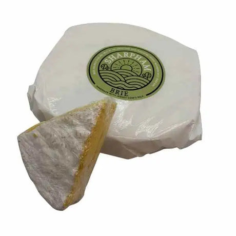 A round white brie cheese wheel wrapped in plastic with a sharpham label featuring sunrises from local dairy farms