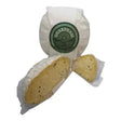 A round rustic sharpham brie wheel wrapped in white paper with green label and two slices showing pale yellow interior speckled with chive and garlic from devon maid artisan local dairy farms