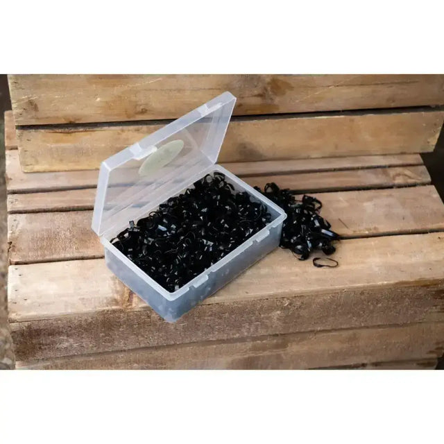 A handy plastic box of black silicone plaiting bands spilling from a plaiting bands tub onto a wooden surface