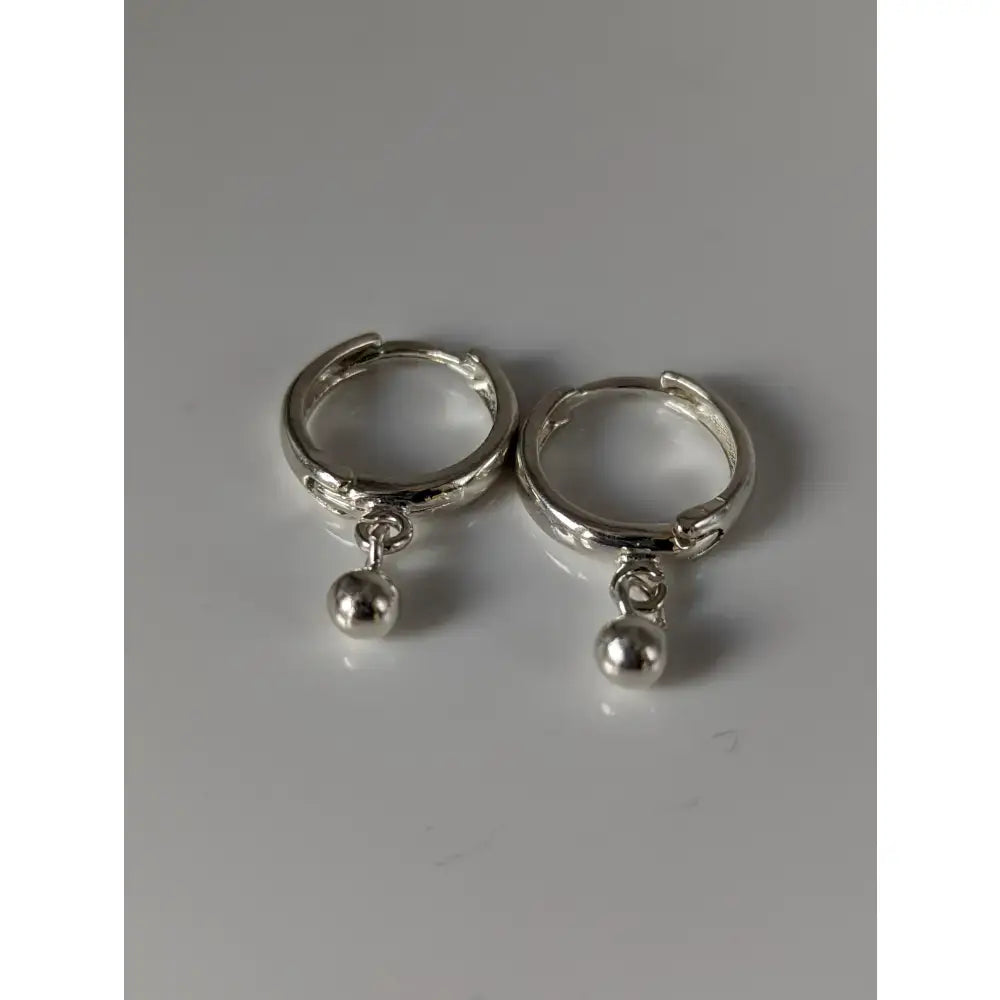 A pair of silver steed ball hoop earrings featuring sleek silver-toned huggie hoops with small spherical charms