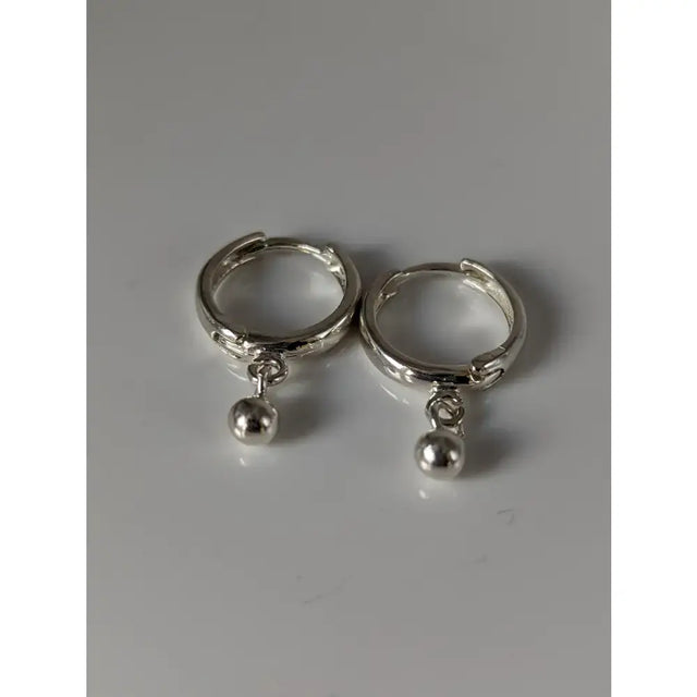 A pair of silver steed ball hoop earrings featuring sleek silver-toned huggie hoops with small spherical charms