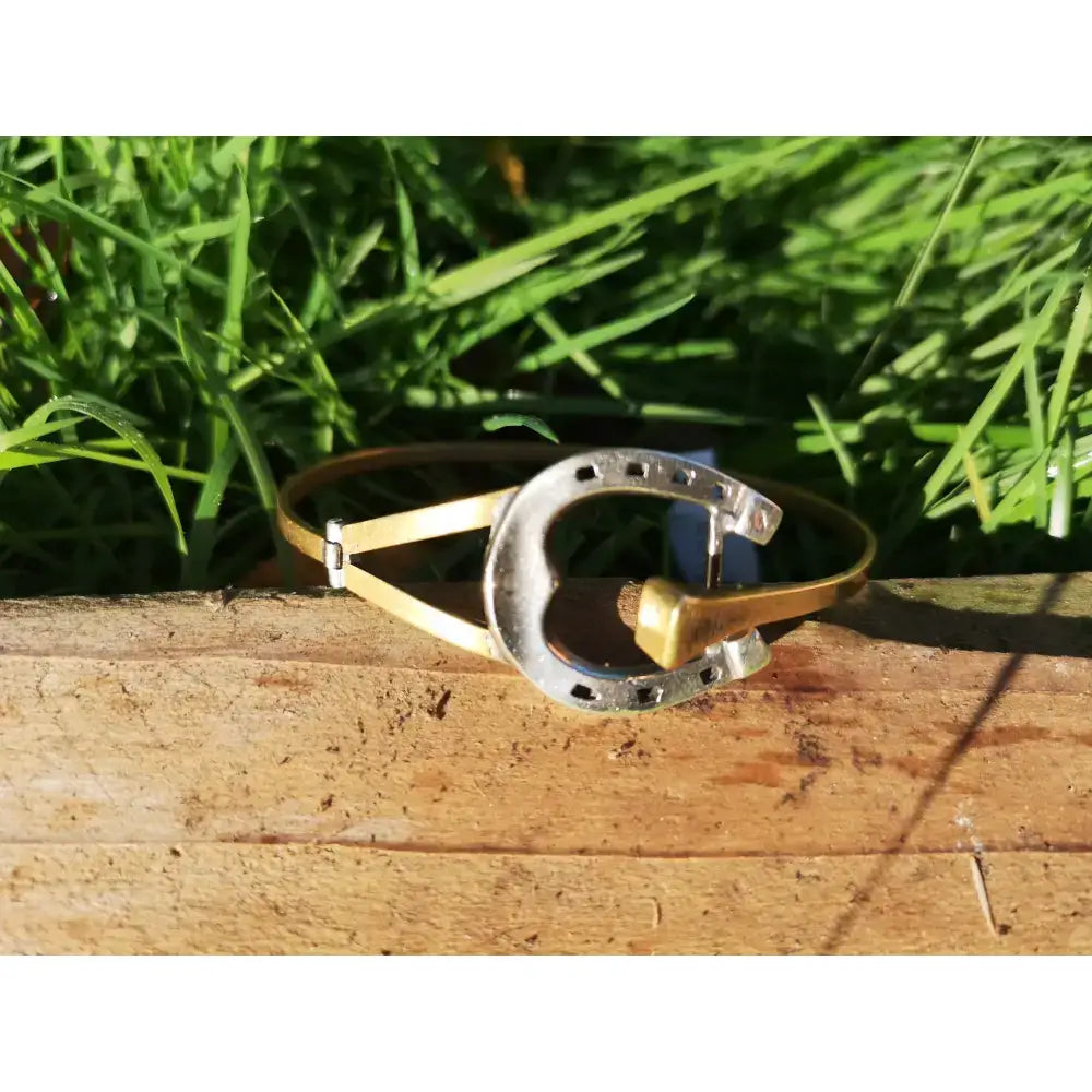 A silver steed big sterling silver horseshoe bangle with gold-tone accents resting on weathered wood