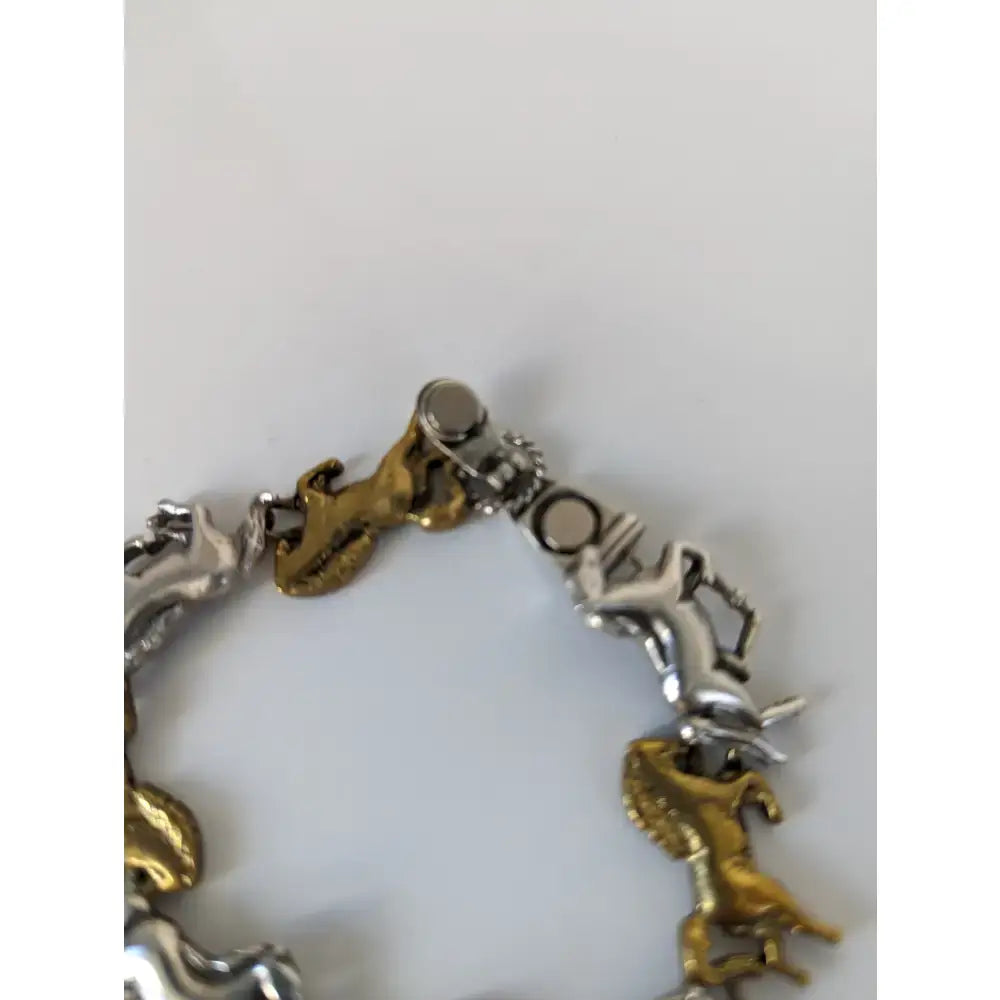 A two-tone silver steed galloping horses bracelet with alternating silver and brass charms and a magnetic clasp