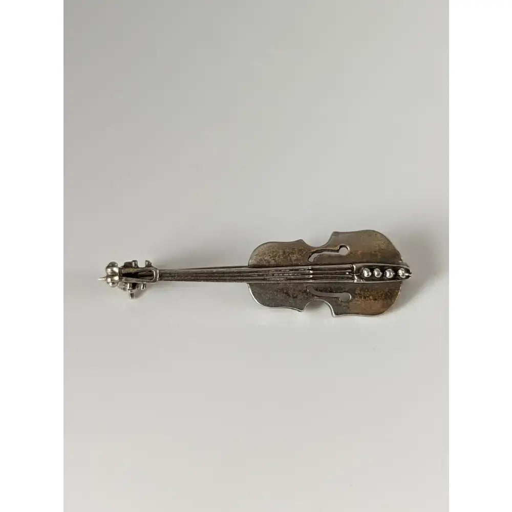 Silver steed cello silver brooch shaped like a violin with intricate detailing and pearl-like embellishments along strings
