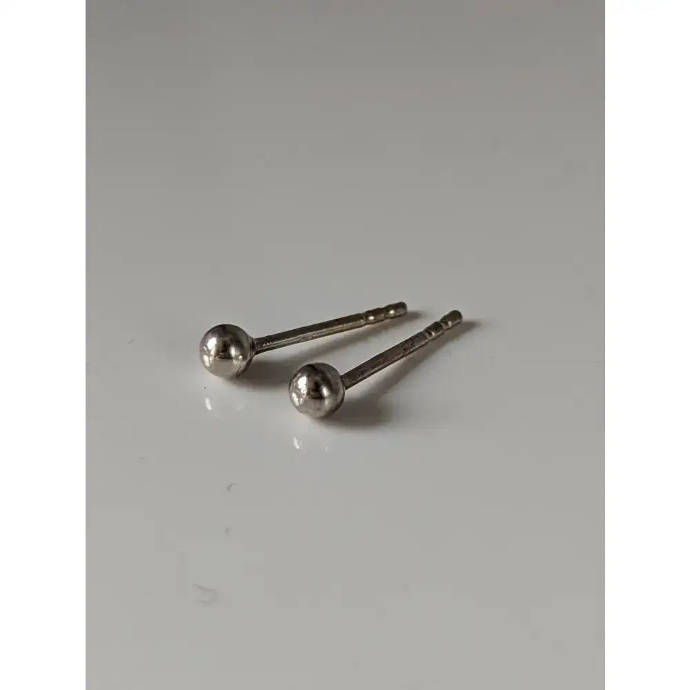 A pair of silver steed ball stud earrings featuring extra small polished silver balls with a unique shape and slender posts