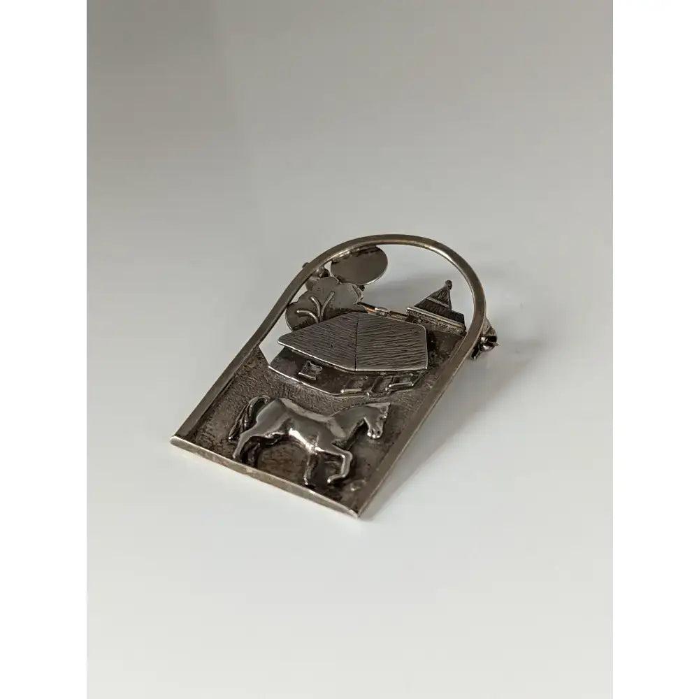 Silver brooch with a detailed silver steed farm relief of horse house and church under an arched frame