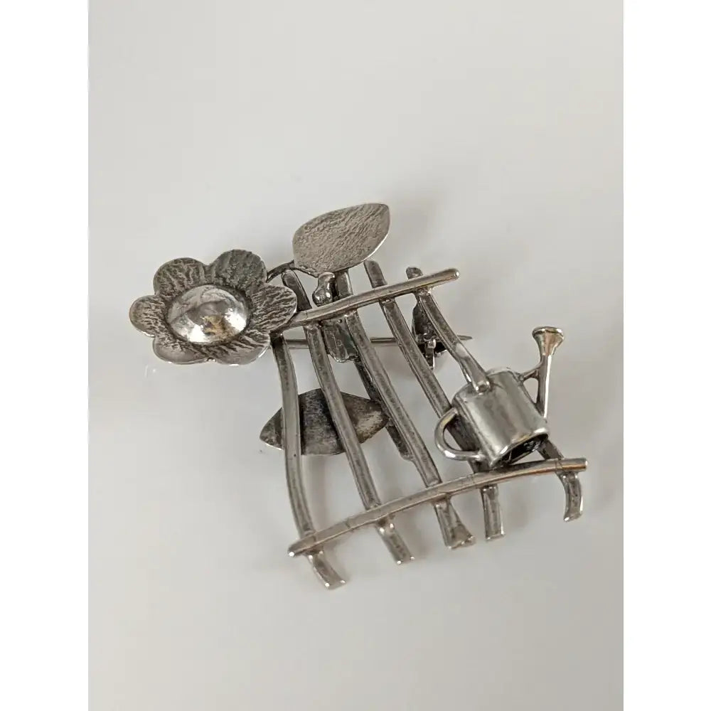 Silver steed garden silver brooch with a flower, clear gemstone center, leaves, and miniature watering can on metal frame