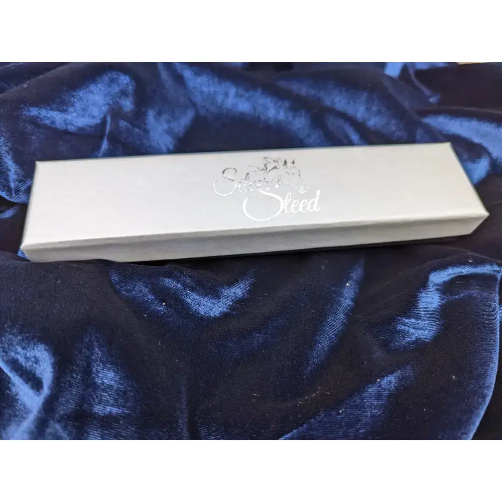 A sleek silver steed gift box with elegant cursive lettering resting on deep blue velvet gift boxes surface